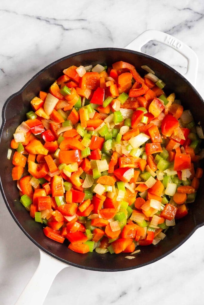 Large enameled cast iron filled with sautéed onions, carrots, celery, and bell peppers.