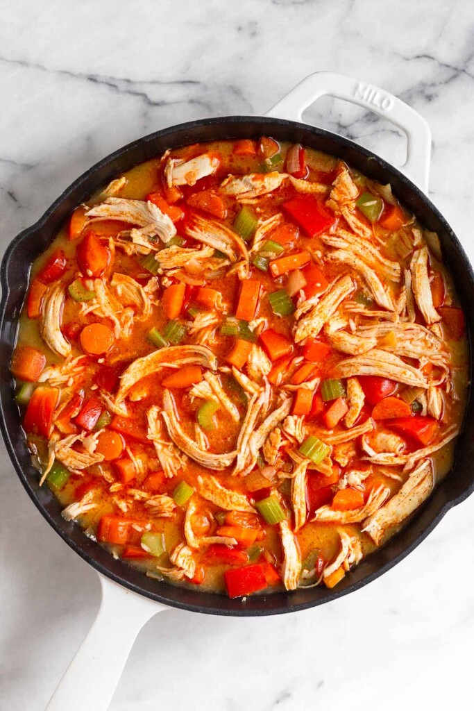 Large enameled cast iron filled with sautéed veggies, shredded chicken, uncooked rice, and broth.