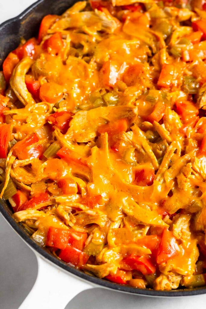 Cast iron skillet filled with chicken, rice, and veggies all cooked together and topped with melted cheese.