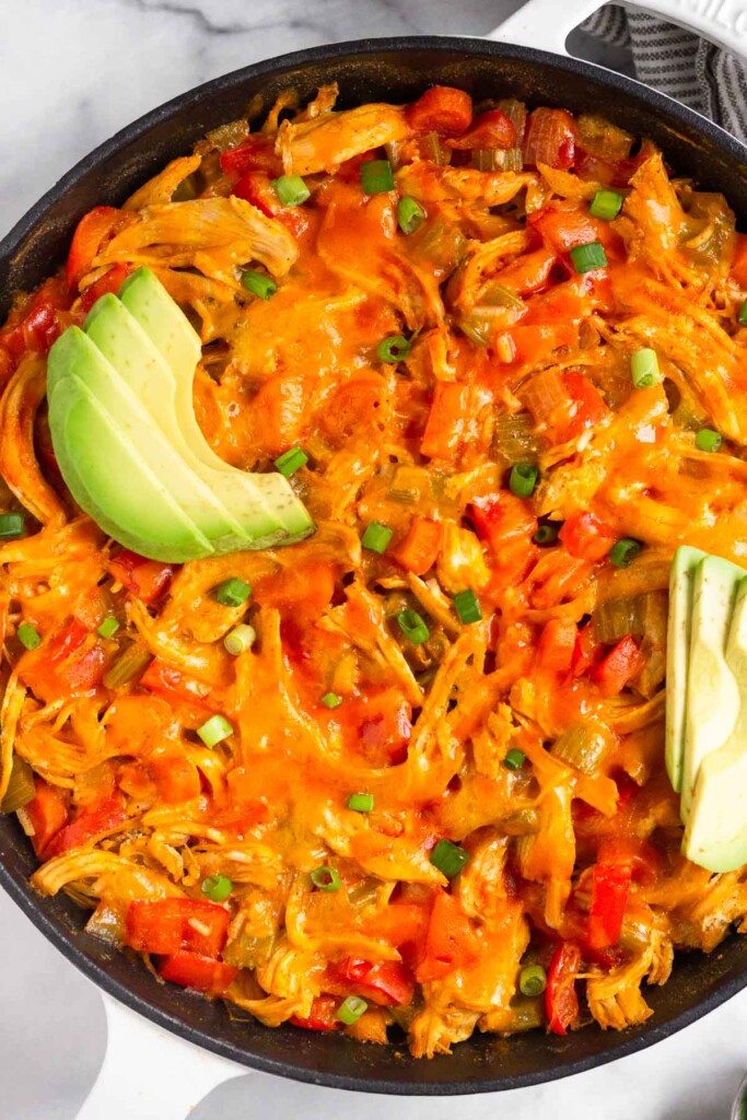 Buffalo chicken casserole in a large cast iron skillet topped with melted cheese, avocado, and green onion.