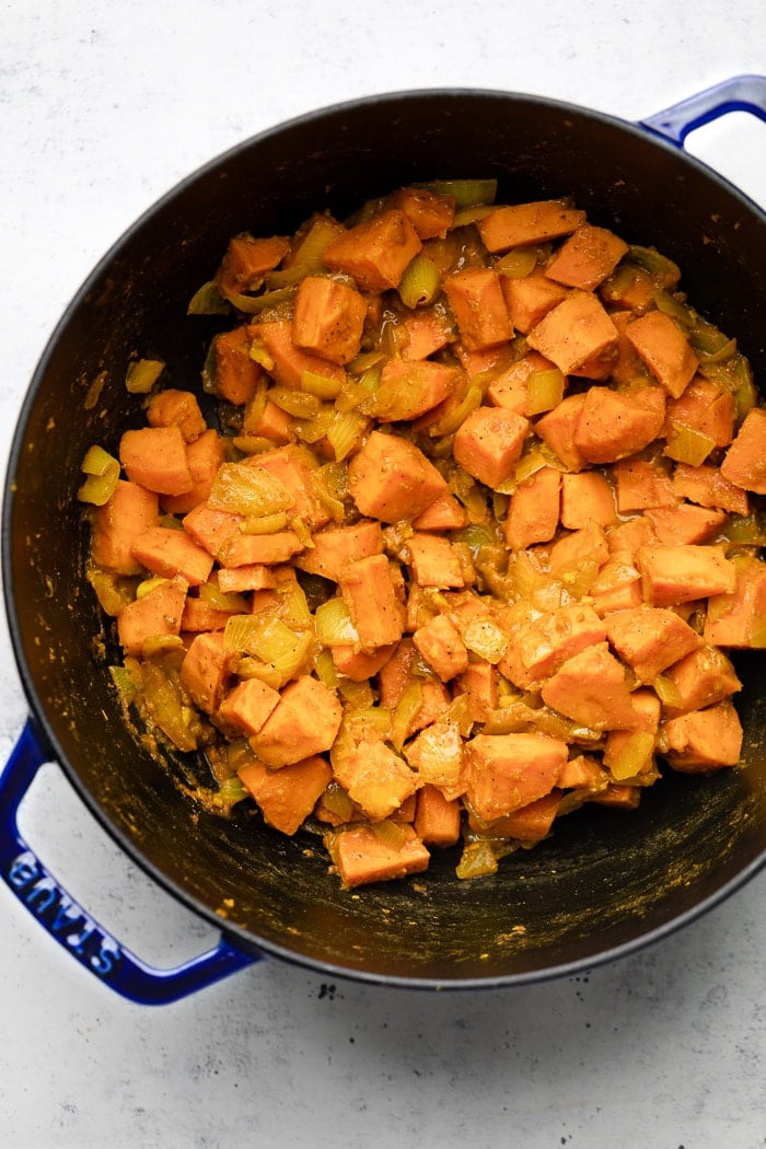 Large dutch oven filled with sautéed sweet potatoes, onion, and spices.