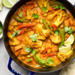 Large dutch oven filled with vegan cauliflower chickpea curry garnished with cilantro. Next to it is lime wedges and a bowl of white rice.