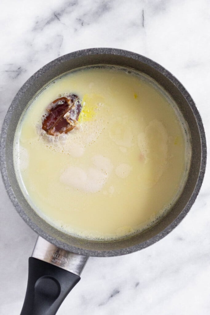 A pot filled with milk with a date and fresh ginger and turmeric. The milk is slightly yellow.