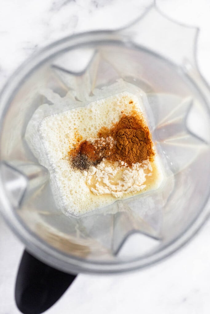 Blender filled with milk, a date, spices, collagen, ginger, and turmeric.