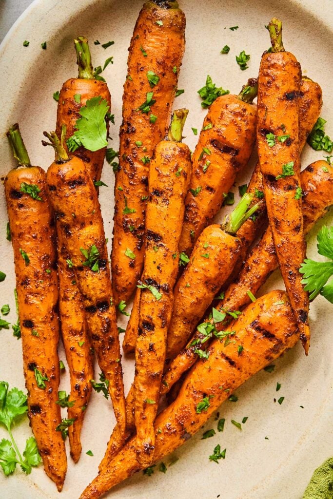 A close up of pile of grilled carrots on a plate. They are topped with chopped cilantro.