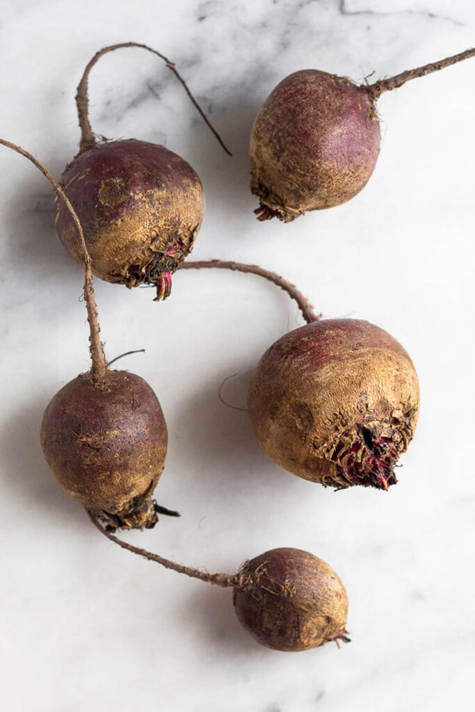 White marble counter with 5 raw red beets on it. The stems have been removed.