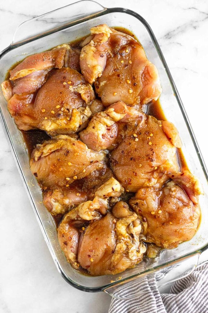 Large glass dish with chicken thighs marinating in spices and coconut aminos in it.