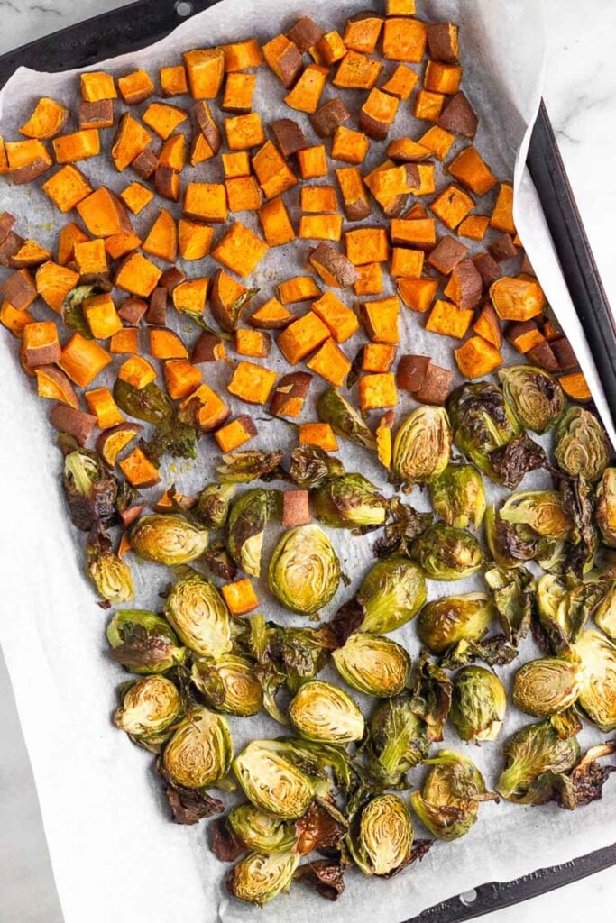 Baking sheet filled with roasted diced sweet potatoes and roasted halved Brussel sprouts.