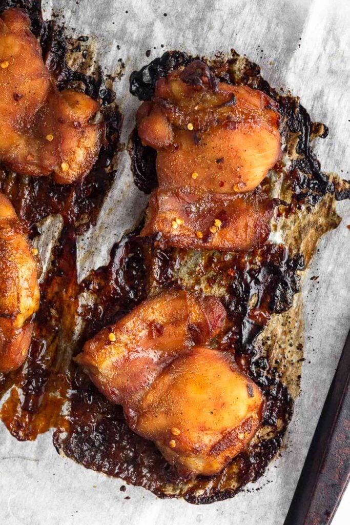 Cooked chicken thighs on a parchment paper lined baking sheet.