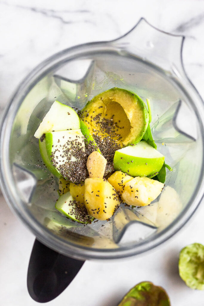Blender filled with spinach, half an avocado, dice green apple, frozen pineapple, ginger root, and chia seeds.