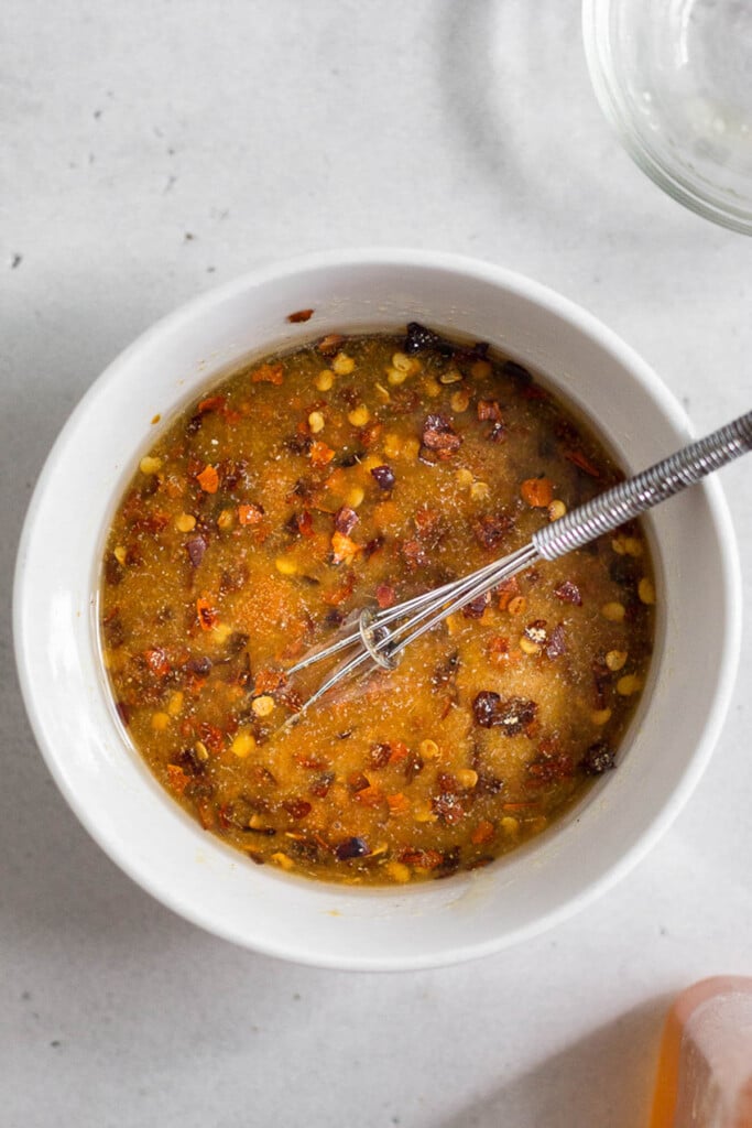 A small bowl with a mixture of honey, coconut aminos, and spices. There is a small whisk in the bowl.