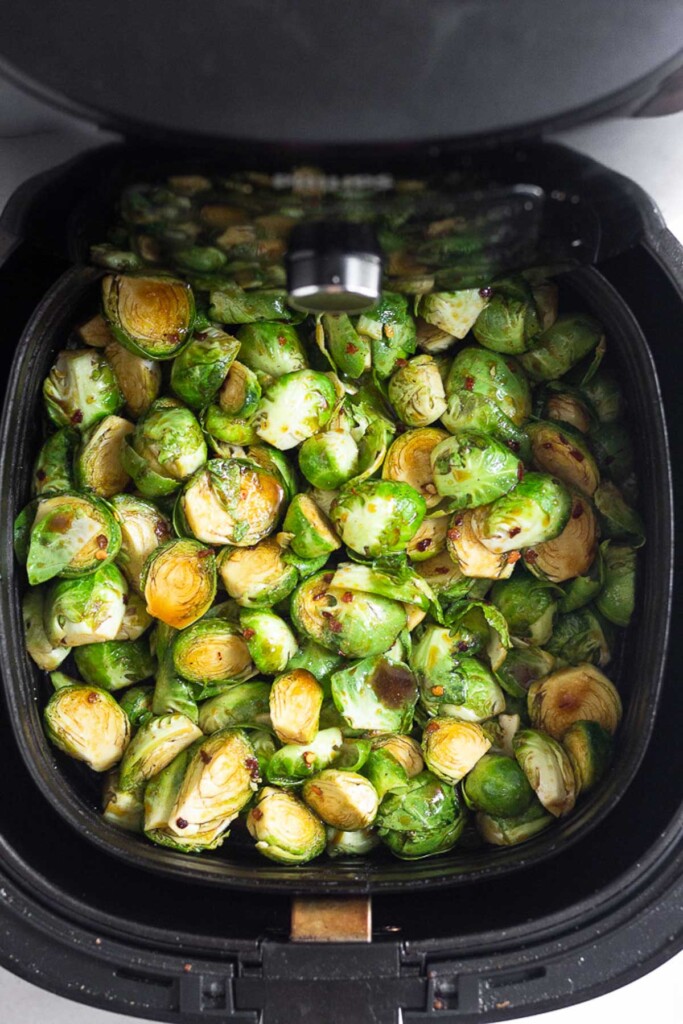 Raw halved brussel sprouts tossed with oil and spices in an air fryer.