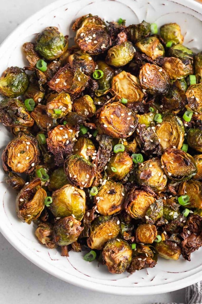 Air fried brussels sprouts in a large white bowl. They are garnished with sesame seeds and green onions.