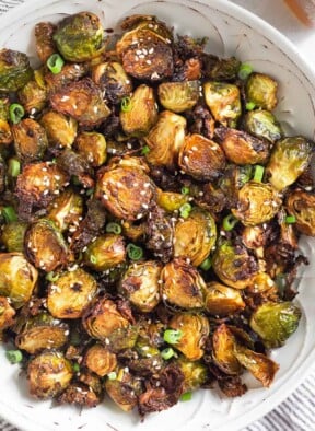 Large white bowl filled with crispy air fryer brussel sprouts garnished with sesame seeds and green onions.
