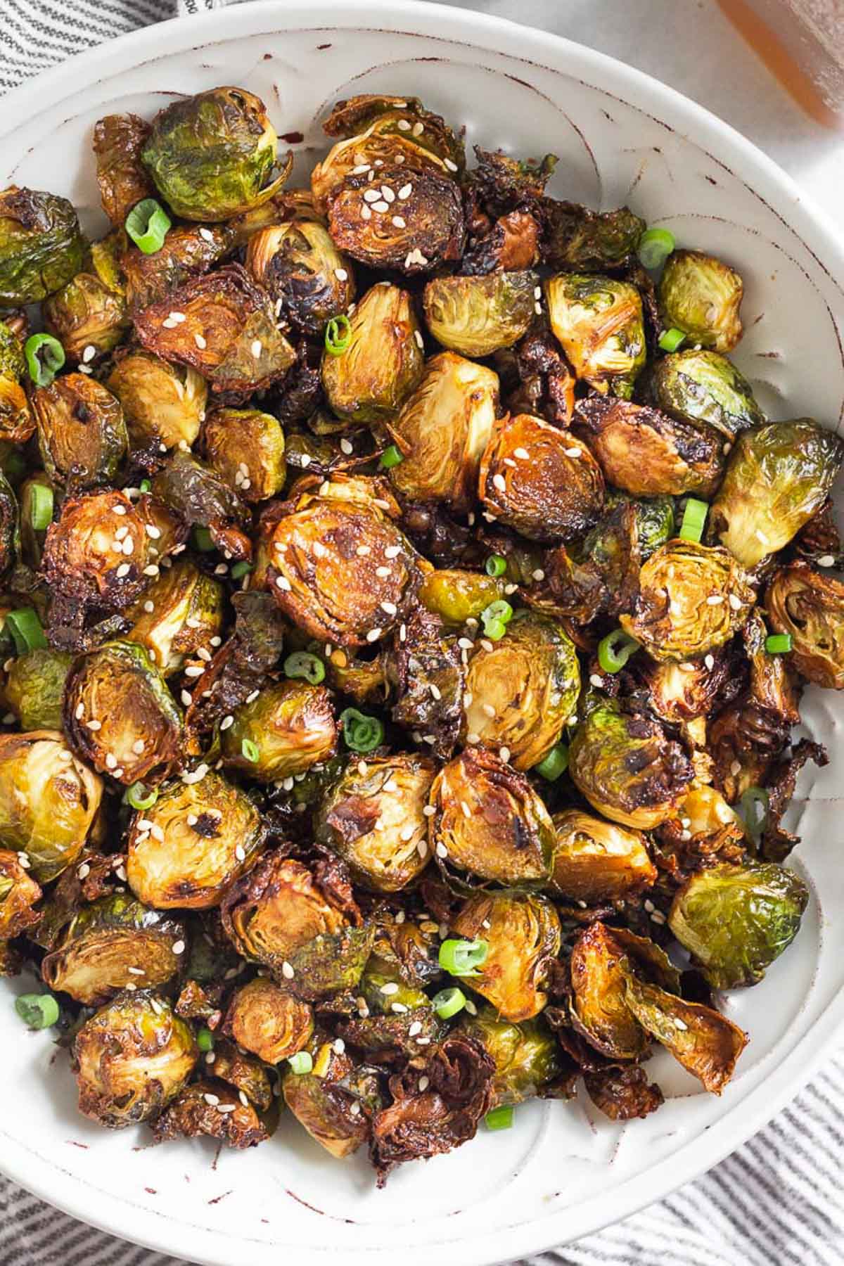 Large white bowl filled with crispy air fryer brussel sprouts garnished with sesame seeds and green onions.