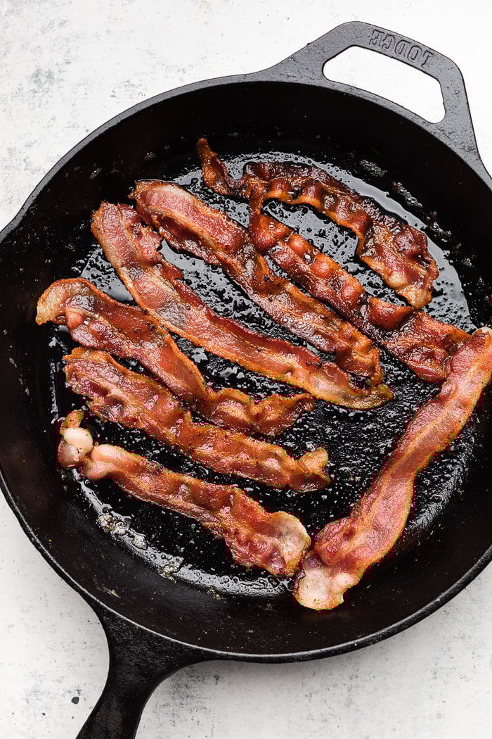 An overhead shot off a large cast iron with cooked bacon in it.