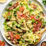 Blt pasta salad on a large white dish and a spoon in it. Around it is s