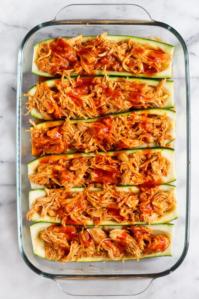 Baked zucchini boats stuffed with buffalo chicken and hot sauce in a pan before they are baked in the oven.
