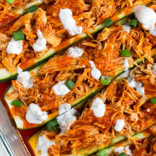 Close up of buffalo chicken zucchini boats topped with blue cheese dressing and green onions.