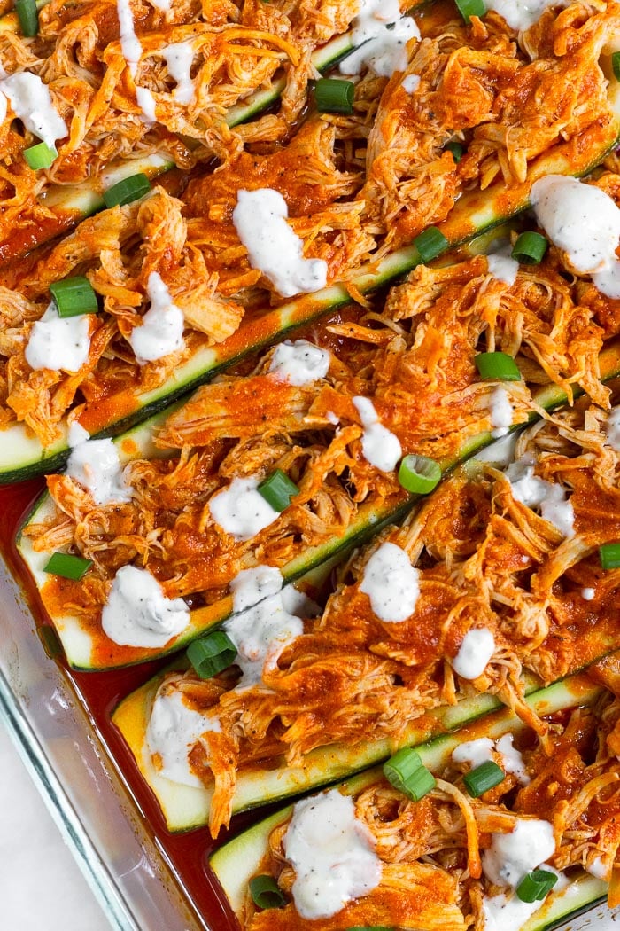 Close up of buffalo chicken zucchini boats topped with blue cheese dressing and green onions.