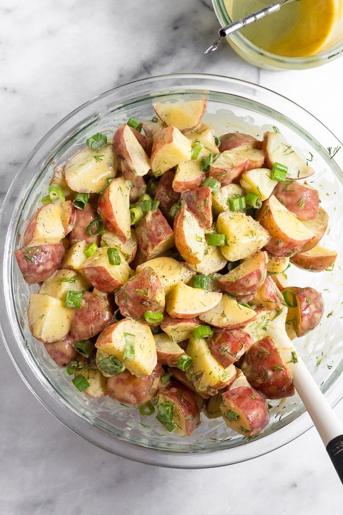 Potato salad with honey mustard dressing recipe in a large glass bowl with a spatula in it. Next to is a jar of honey mustard dressing.