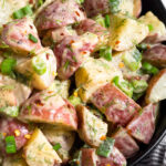 Close up of honey mustard potato salad in a bowl topped with green onions and red pepper flakes.