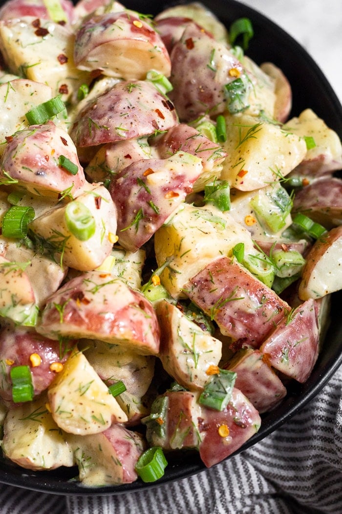 Close up of honey mustard potato salad in a bowl topped with green onions and red pepper flakes.