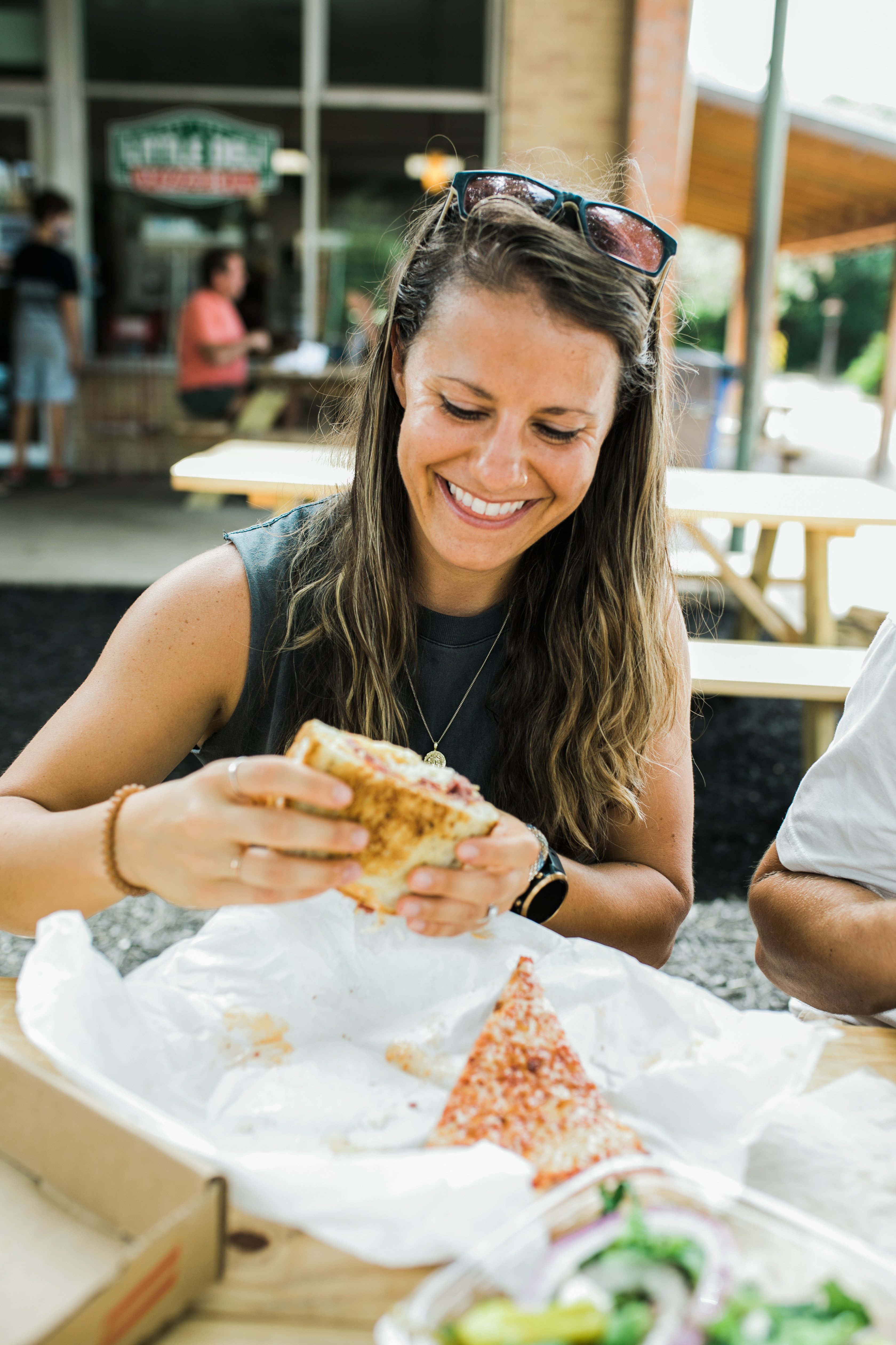 Woman holding a large sandwich that she is about to take a bite of. She is smiling down at it.