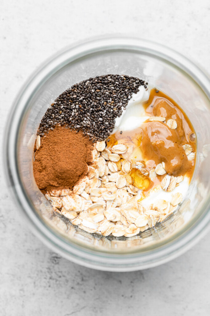 An overhead shot of a jar with rolled oats, cinnamon, chia seeds, greek yogurt, cashew butter, and honey before it is mixed up.