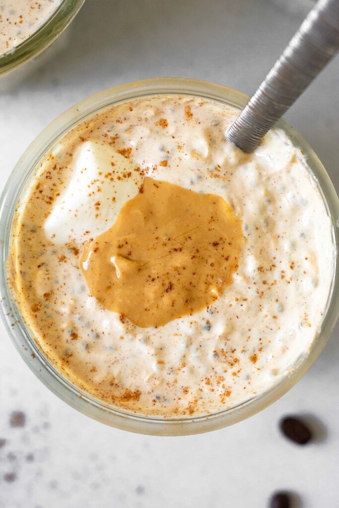 Overhead shot of a jar of overnight oats topped with greek yogurt, cashew butter, and cinnamon. A spoon is in the jar.
