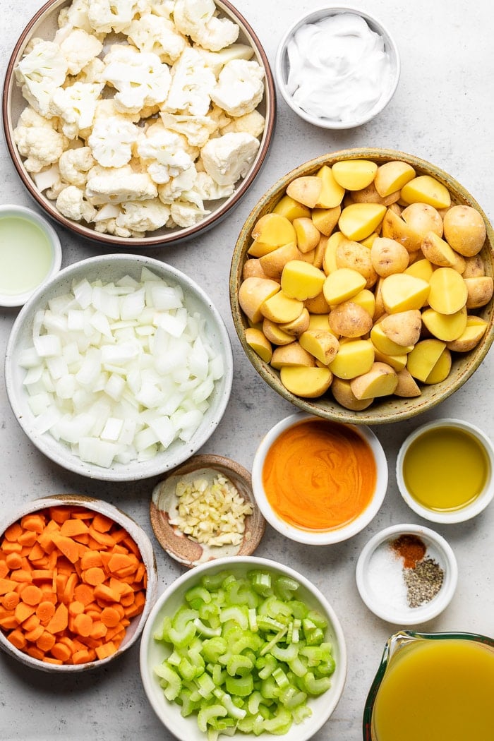 Overhead shot of a bunch of different bowls filled with different things. There cauliflower florets, coconut milk, potatoes, oil, buffalo sauce, spices, broth, celery, onions, carrots, garlic, and lemon juice.