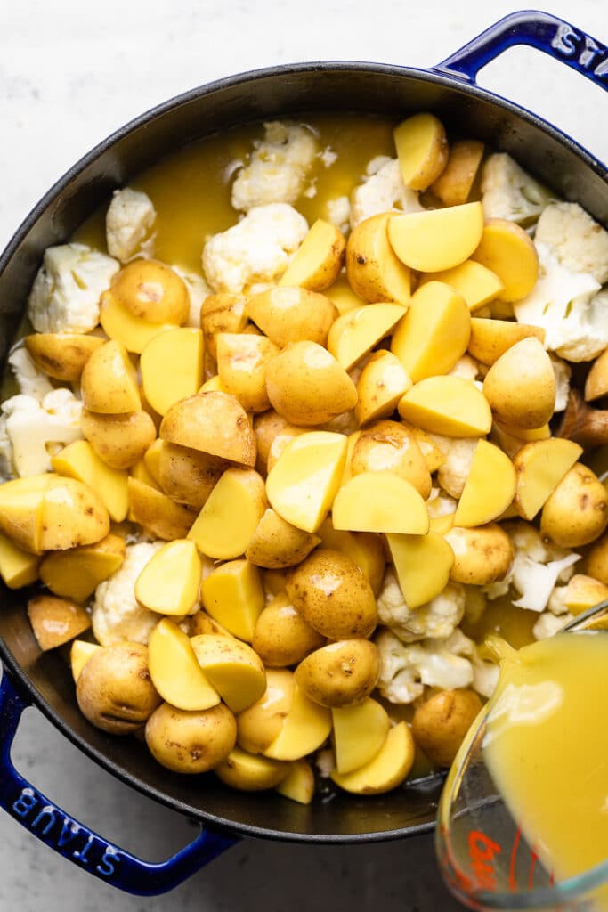 Large stock pot filled with cauliflower and potatoes with broth being poured into it.