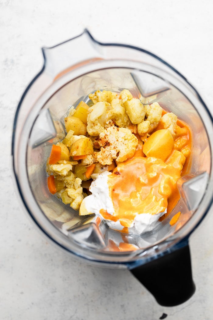 Blender filled with cauliflower, potatoes, coconut milk, and buffalo sauce.