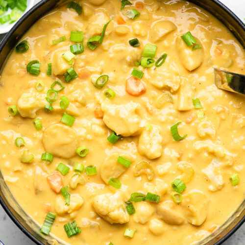 Large pot of vegan buffalo cauliflower potato soup garnished with green onions. Around it is a small bowl of green onions and a bowl of buffalo sauce.