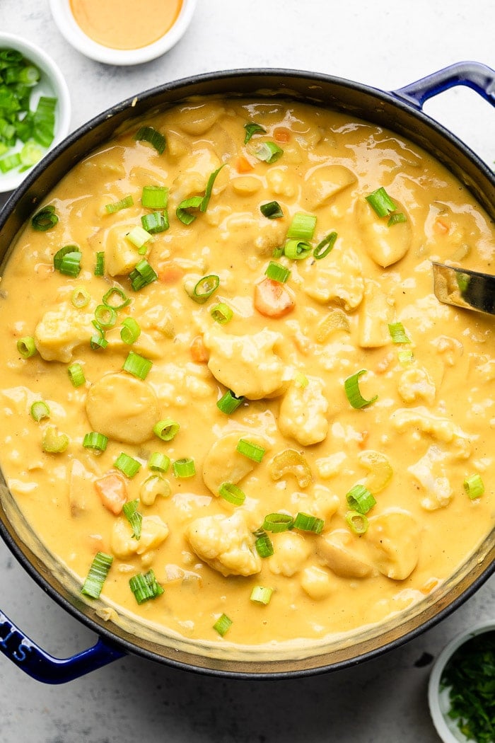 Large pot of vegan buffalo cauliflower potato soup garnished with green onions. Around it is a small bowl of green onions and a bowl of buffalo sauce.