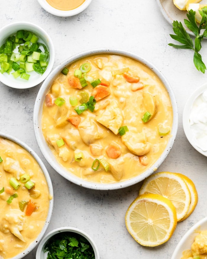 Bowl filled with buffalo cauliflower soup. it is garnished with green onions. Around it is another bowl of soup, bowl of green onions, and sliced lemons.