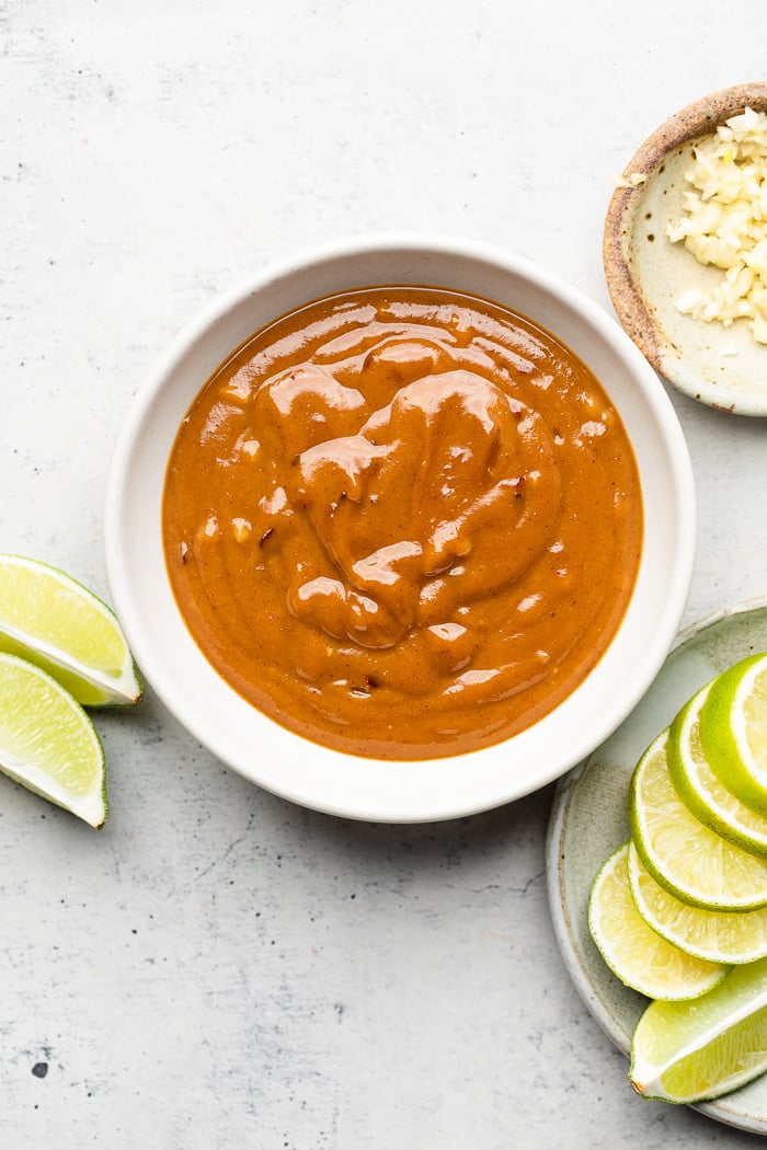 Overhead shot of a bowl of peanut butter sauce. Next to it are lime wedges and a bowl of minced garlic.