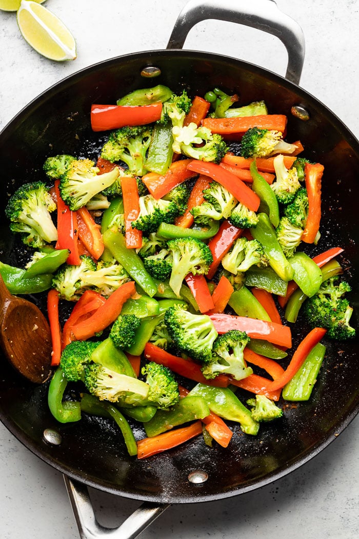 Large saute pan filled with sautéed peppers and broccoli. Next to it are a few lime wedges.