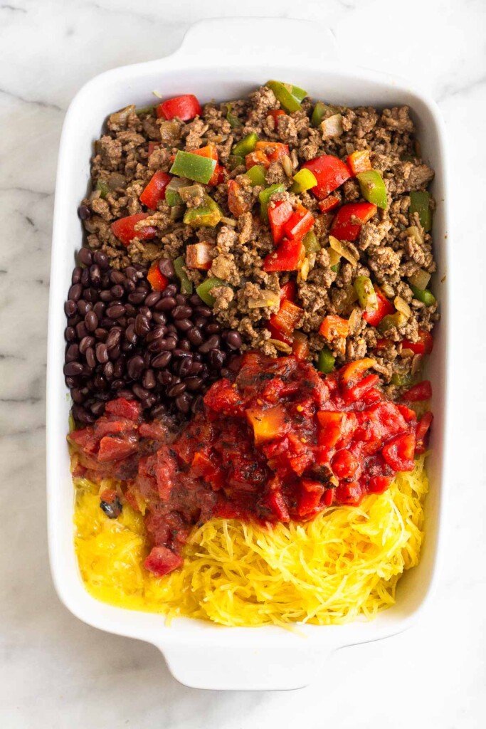 Large casserole dish filled with a pile of cooked spaghetti squash, scrambled eggs, diced tomatoes, black beans, and a mixture of cooked ground beef and veggies.