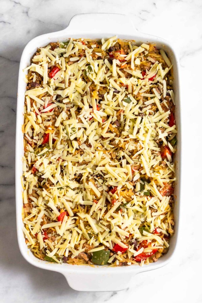 Large casserole in a dish sprinkled with shredded cheese before it is baked.