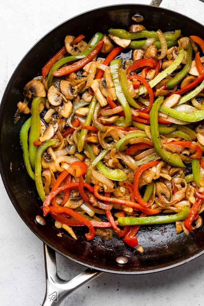 Large skillet filled with sautéed onions, peppers, and mushrooms.