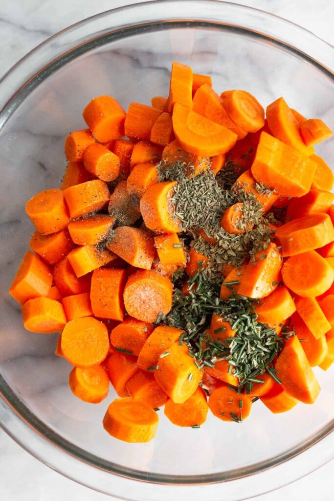 Chopped raw carrots in a large bowl topped with oil and herbs.