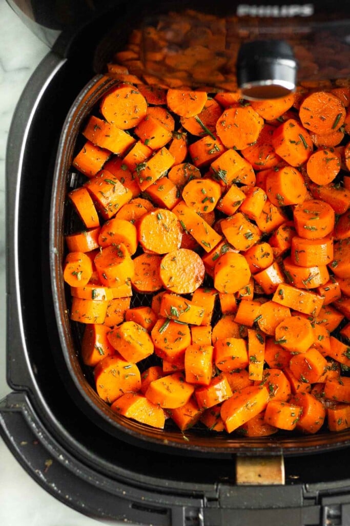 Chopped raw carrots tossed with oil and herbs in an air fryer basket..