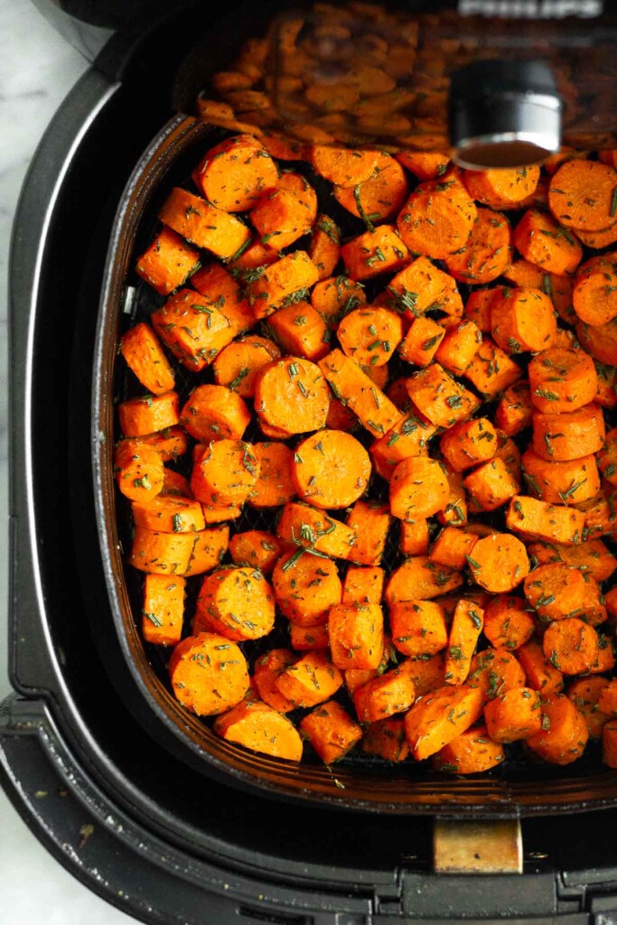 Air fryer basket filled with seasoned chopped carrots halfway through cooking.