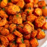 Close up of air fryer carrots on a white plate garnished with fresh herbs.