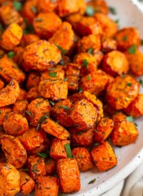Close up of air fryer carrots on a white plate garnished with fresh herbs.