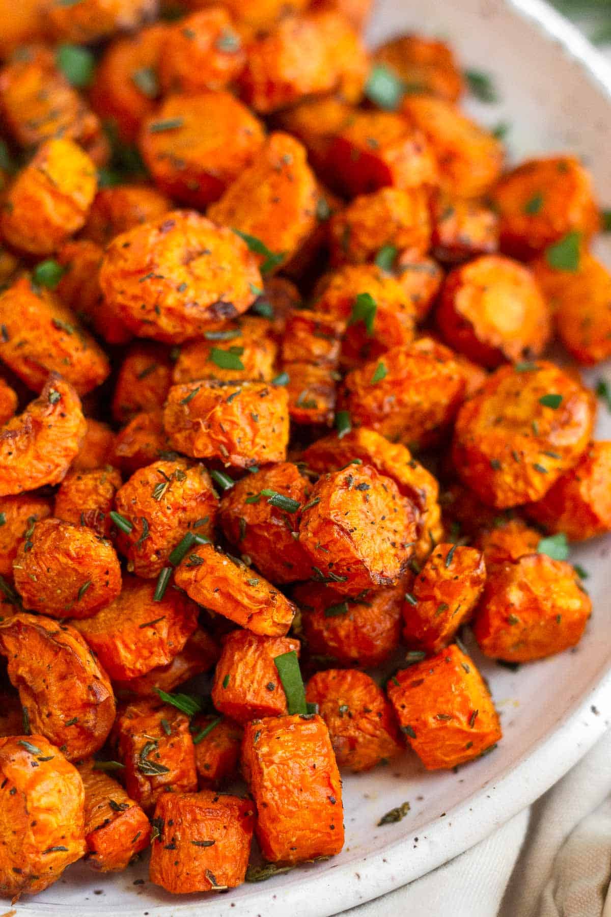 Close up of air fryer carrots on a white plate garnished with fresh herbs.