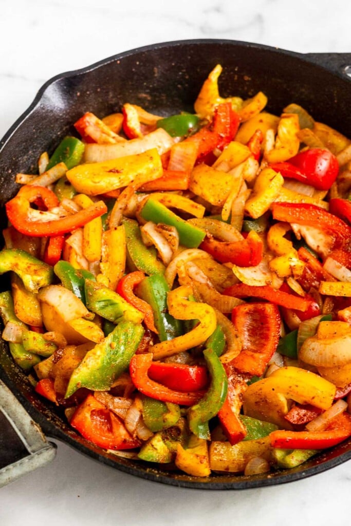 Large cast iron skillet filled with sautéed peppers and onions.