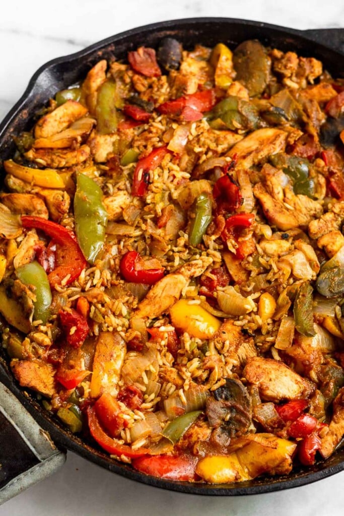 Large cast iron filled with chicken and rice casserole with peppers, onions, and mushrooms.
