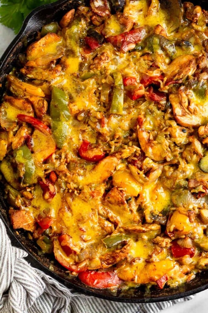 Overhead shot of baked chicken fajita casserole topped with melted cheese in a large cast iron skillet.